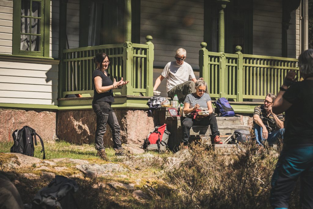 Amanda med en turistgrupp utanför en grön somrig veranda.